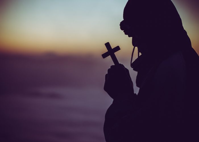 concept of religion. Silhouette of a man praying with a cross in hand at sunrise.