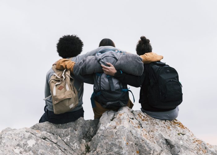 three-friends-with-their-arms-around-sitting-top-mountain